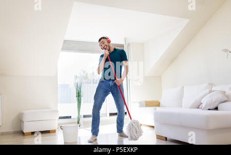 man in headphones singing to by mop at home Stock Photo