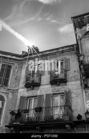 Visual illusion of Sun entering a house through the chimney in North Italy. Airplane contrail. Street view, black and white image. Stock Photo