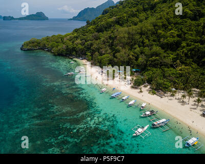 Aerial drone view of traditional Banca boats and coral reef surrounding a scenic tropical sandy beach (7 Commando Beach, El Nido) Stock Photo
