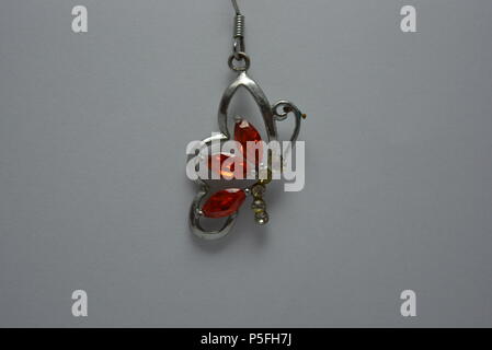 Jewelry, women's metal earrings with red, orange stone located on white background. Stock Photo