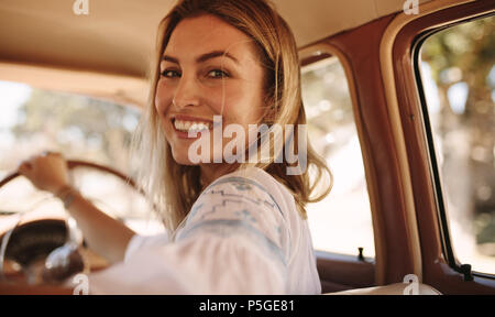 Close up portrait of smiling young woman sitting on a driving seat of a vintage car. Beautiful female driving a old car. Stock Photo