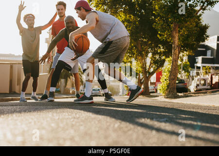 Men playing basketball game on a sunny day on an empty street. Men practicing basketball dribbling skills on street. Stock Photo