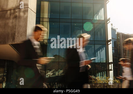 Business people using mobile phones while commuting to office. People busy with mobile phones while walking on street. Stock Photo