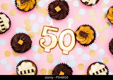Number 50 gold candle with cupcakes against a pastel pink background Stock Photo