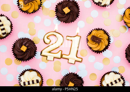 Number 21 gold candle with cupcakes against a pastel pink background Stock Photo