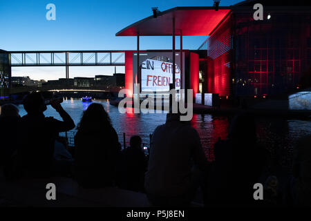 26 June 2018, Germany, Berlin: Several people follow the large-scale projection 'Dem deutschen Volke' (lit. 'to the German People') at the banks of the River Spree in the government district. As soon as night sets in, the history of the parliamentary democracy in Germany is shown in image, film and sound. Photo: Paul Zinken/dpa Stock Photo