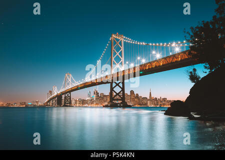 Classic panoramic view of San Francisco skyline with famous Oakland Bay Bridge illuminated in beautiful evening twilight at dusk in summer