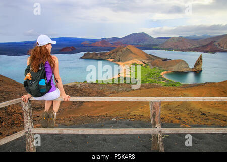 Young woman enjoying the view of Pinnacle Rock on Bartolome island, Galapagos National Park, Ecuador. This island offers some of the most beautiful la