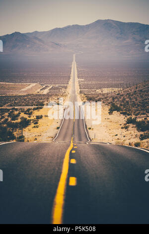 Classic panorama view of an endless straight road running through the barren scenery of the American Southwest with extreme heat haze on a beautiful s Stock Photo