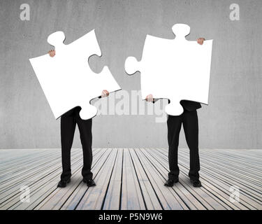 Businessmen holding two puzzles to connect on wooden floor Stock Photo