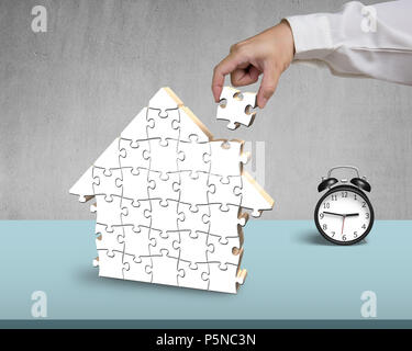Assembling blank wooden puzzles in house shape on desk Stock Photo