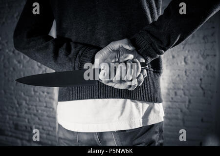 close up of a hands holding a knife of dangerous hooded man standing in the dark in London knife crime concept. Stock Photo