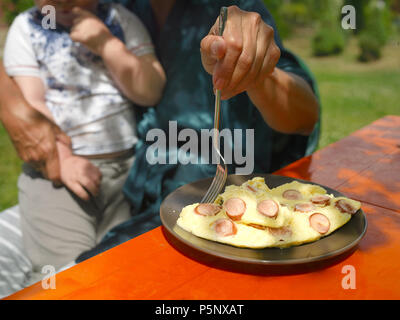 Hand with fork oicking a piece of fried eggs trying to feed a child sitting on the mom knees Stock Photo