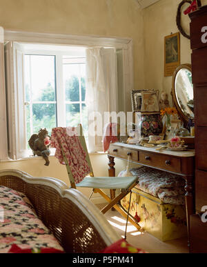 Canvas+wood vintage chair at cluttered marble-topped dressing table in cottage bedroom with white shutters on window Stock Photo