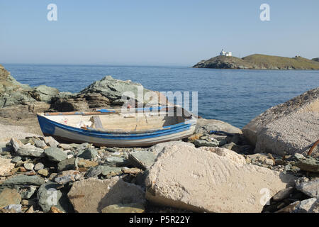 Small Boat Moored on the Rocky Shore on the Island of Kea ( Tzia ) with Lighthouse in the distance, Aegean Sea’s Cyclades archipelago, Greece. Stock Photo