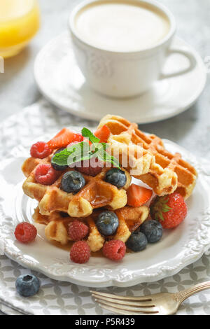 Fresh homemade waffles with raspberries, strawberries, blueberries and honey. Delicious Breakfast with berries, cappuccino and orange juice . Selectiv Stock Photo