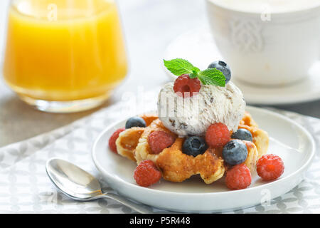 Homemade waffles with ice cream and fresh berries-raspberries, blueberries. Delicious dessert, cappuccino and orange juice on the table. Selective foc Stock Photo