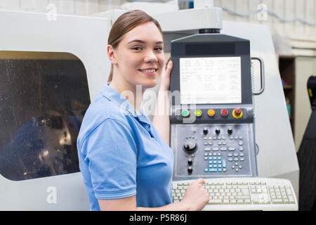 Portrait Of Female Apprentice Engineer Operating CNC Machine In Factory Stock Photo