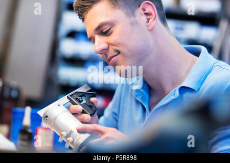 Male Apprentice Measuring Component In Factory Stock Photo
