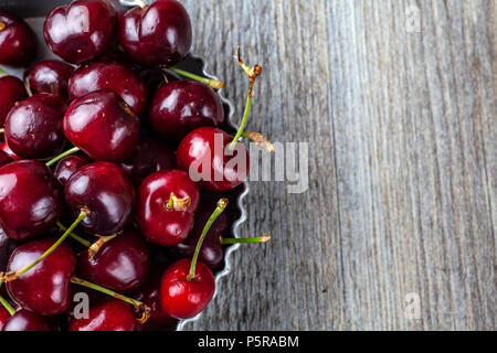 Less than perfect red cherries in a tin dish on a wooden table Stock Photo