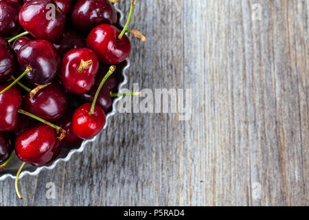 Less than perfect red cherries in a tin dish on a wooden table Stock Photo