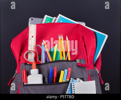 Closeup of a book bag with an assortment of school supplies on a blackboard background Stock Photo