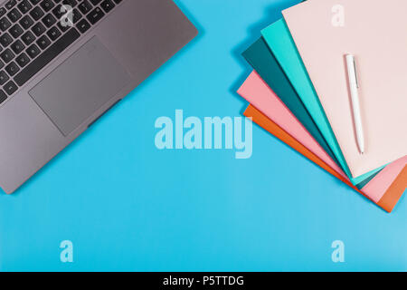 Workspace with laptop keyboard and colorful notebooks on blue background. Stock Photo