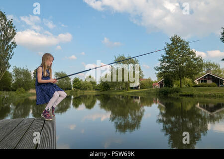 A 7 year old girl is sitting by a lake with fishing rod and looking at the  water. She waits for a fish to bite Stock Photo - Alamy