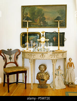 Antique paintings on wall above painted vintage console table in hall with antique chair and dolls Stock Photo