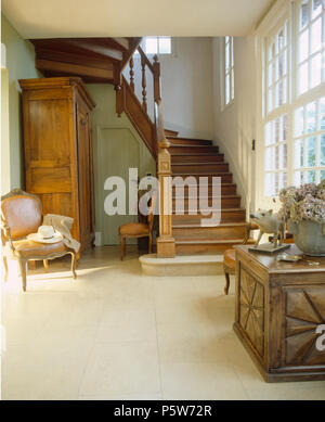 Antique chair and cupboard in French country hall with stone tiled floor and oak staircase Stock Photo