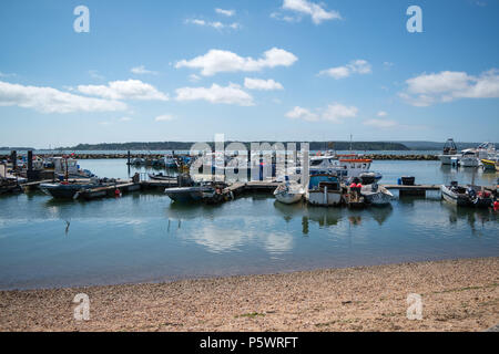 Looking out over the calm waters and fisherman's boats berthed in Poole Harbour on a bright sunny day with Brownsea Island in the distance. Stock Photo