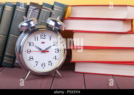 Science and education -  alarm clock and pile group of colorfull books on the wooden table and yellow background. Stock Photo