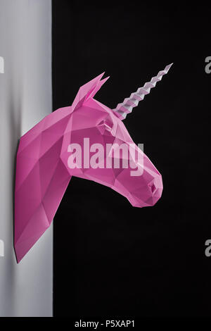 Pink saturated geometrical unicorn's head hanging on grey wall. Black background. Innovative interior design details. Straight lines. Original geometrical shape. Shadows. Decorations shooting. Stock Photo