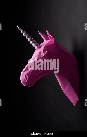 Bright pink unicorn's head hanging on black saturated wall. Black background. Innovative interior design details. Straight lines. Original geometrical shape. Shadows. Decorations shooting. Stock Photo