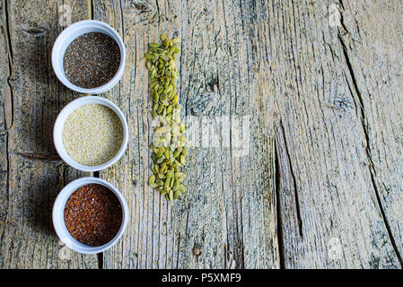 Three super foods chia, flax and sesame seeds in white pals on a wooden background, and next to the seeds of pumpkin. Top view. Stock Photo