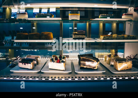 Showcase with a variety of cakes and pastries. Small glass fridge shelves with desserts in stylish dark blue interior of the cafe. Stock Photo