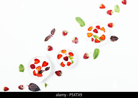 Three bowls of strawberry ice cream on a white background, top view. Flat lay concept arrangement of summer cold refreshing desserts decorated with re Stock Photo