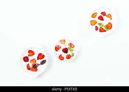 Three bowls of strawberry ice cream on a white table, top view. Flat lay composition of cold desserts decorated with fresh red berries and mint and pu Stock Photo