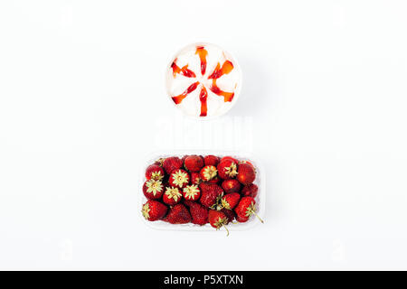 Ice cream with topping syrup and a box of fresh strawberries, top view. Flat lay minimal composition of frozen dessert and red berries on a white back Stock Photo
