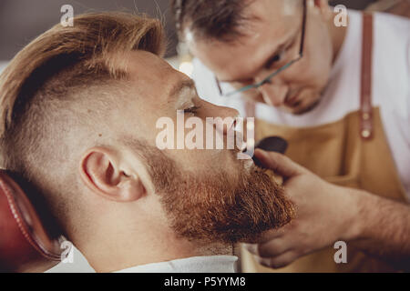 Man in the process of trimming a beard in a barbershop.  Photo in vintage style Stock Photo