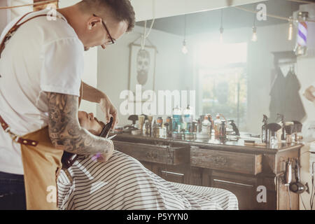 Barber cuts the client's beard in his barber shop. Photo in vintage style Stock Photo