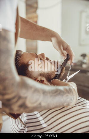 Barber cuts the client's beard with scissors and a comb. Photo in vintage style Stock Photo