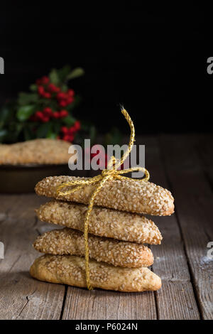 Sicilian biscuits with sesame seeds tight with golden bow and decorated with red berries for winter holidays. Stock Photo