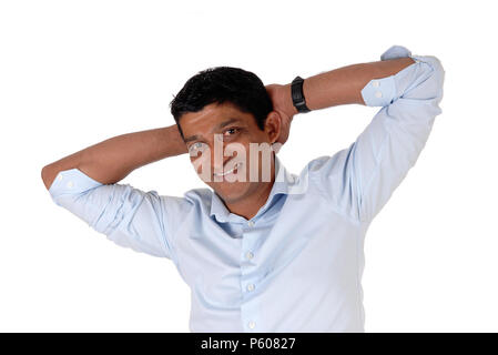 A smiling East Indian man in closeup standing in a blue shirt with his hands behind his head, isolated for white background Stock Photo