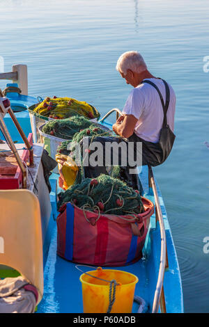 Local fisherman repairing the fishing nets on a traditional styled fishing boat tied up in the old harbour at Ayia Napa, Cyprus Stock Photo