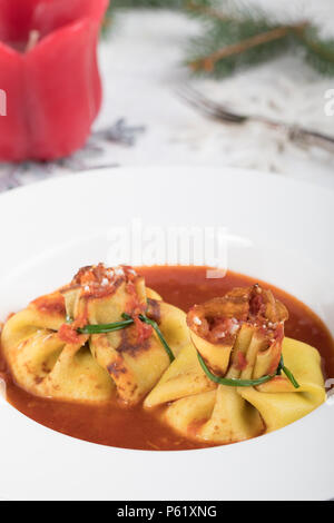 Closeup of a plate with baked fagottini pasta filled with ricotta cheese and tight with fresh chives, on tomato sauce, a traditional plate. Stock Photo