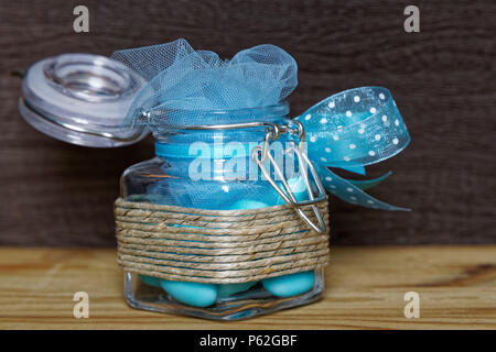 Decorative jar with bow and blue stones inside on wooden table, mockup for postcard or greeting card. Stock Photo