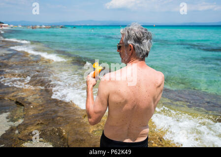 Senior man applying sun lotion on summer vacation back view Stock Photo