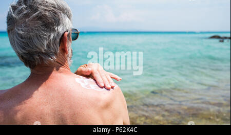Senior man applying sun lotion on summer vacation back view Stock Photo