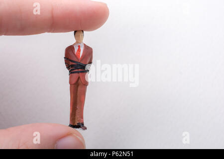 Hand holding tiny figurine of man model tied in a rope Stock Photo